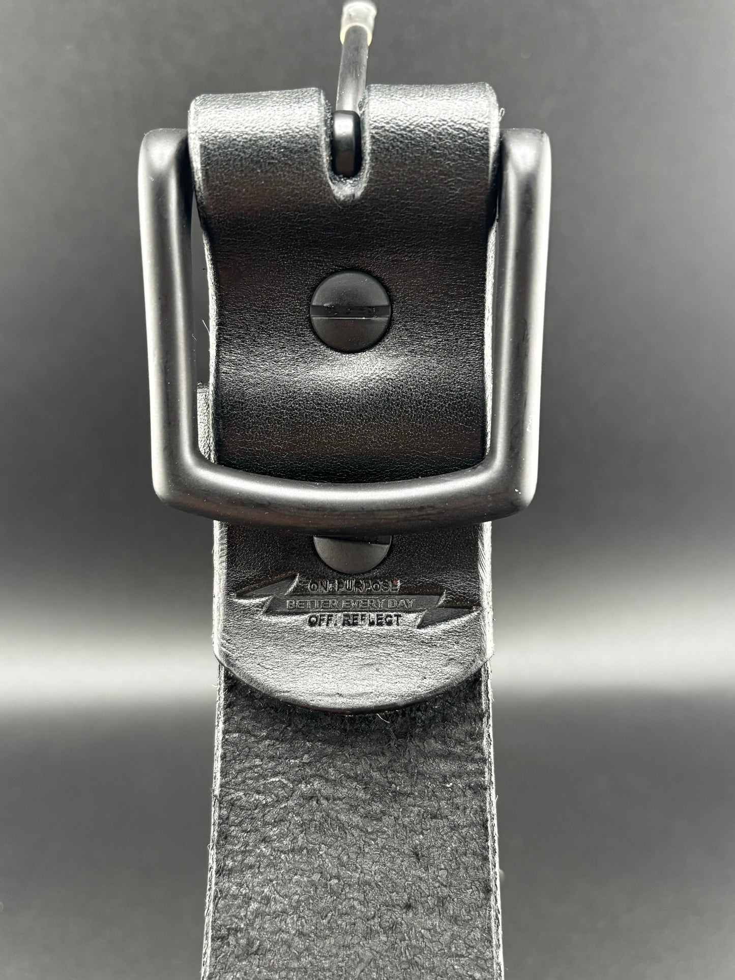 Close-up of a black leather belt with a metal buckle on a gray background