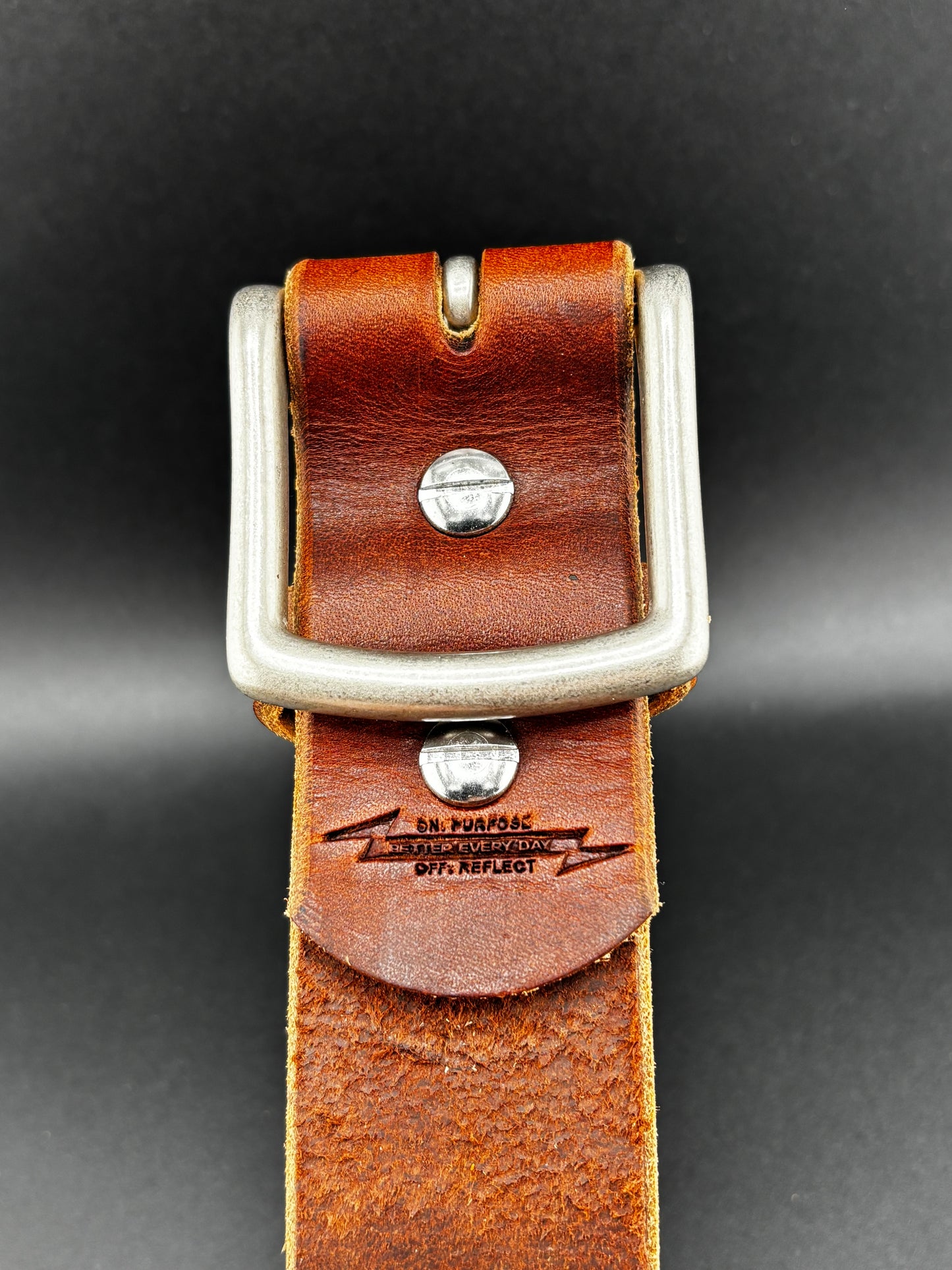 Brown leather belt with silver buckle on a dark background