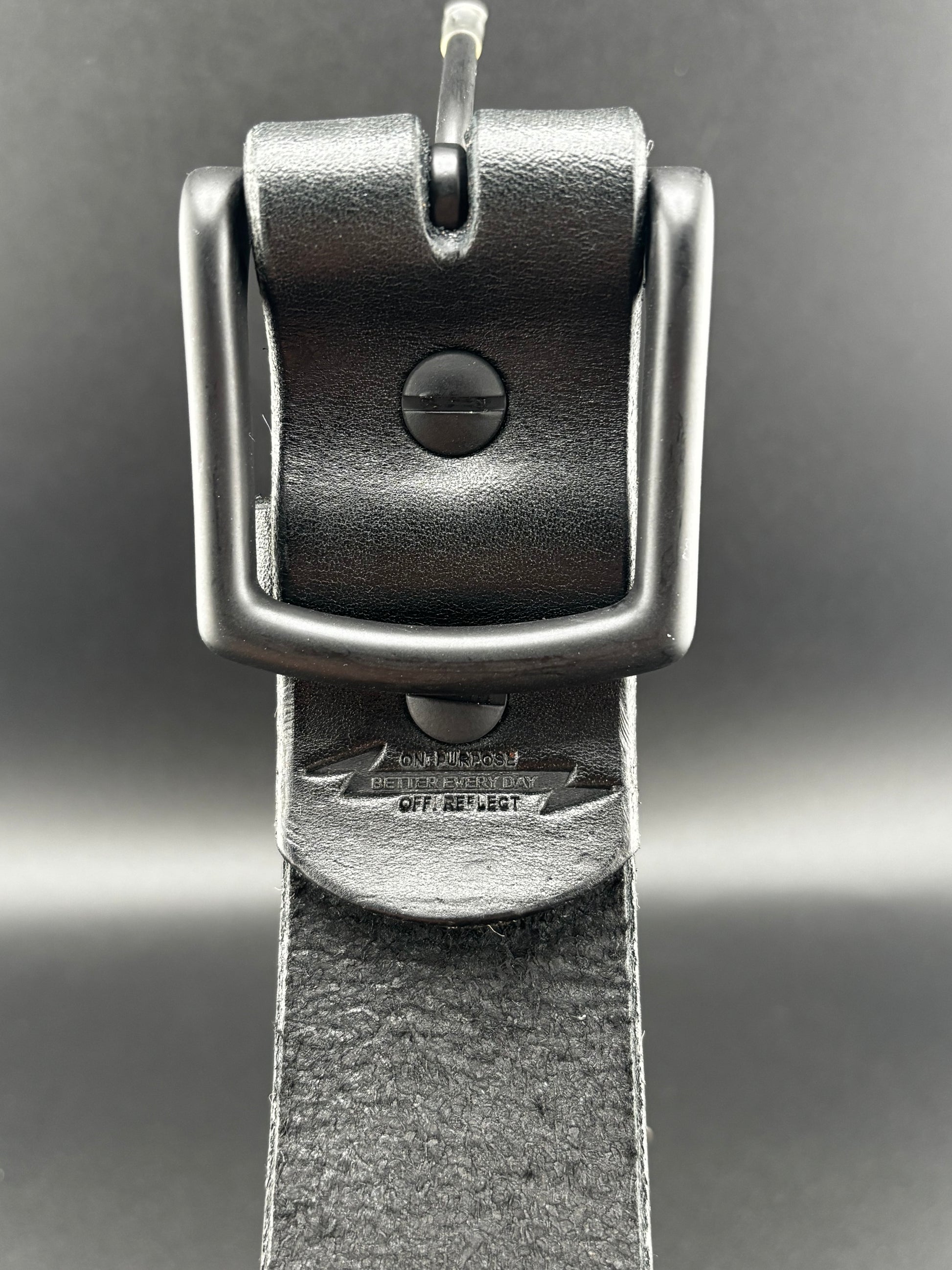 Close-up of a black leather belt with a metal buckle on a gray background