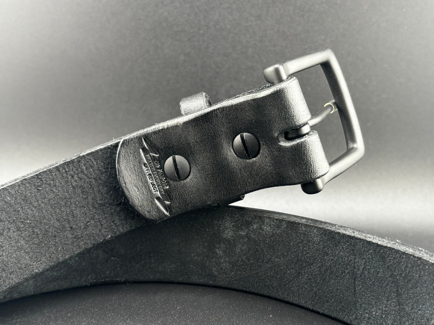 Close-up of a black leather belt with a black buckle on a dark background
