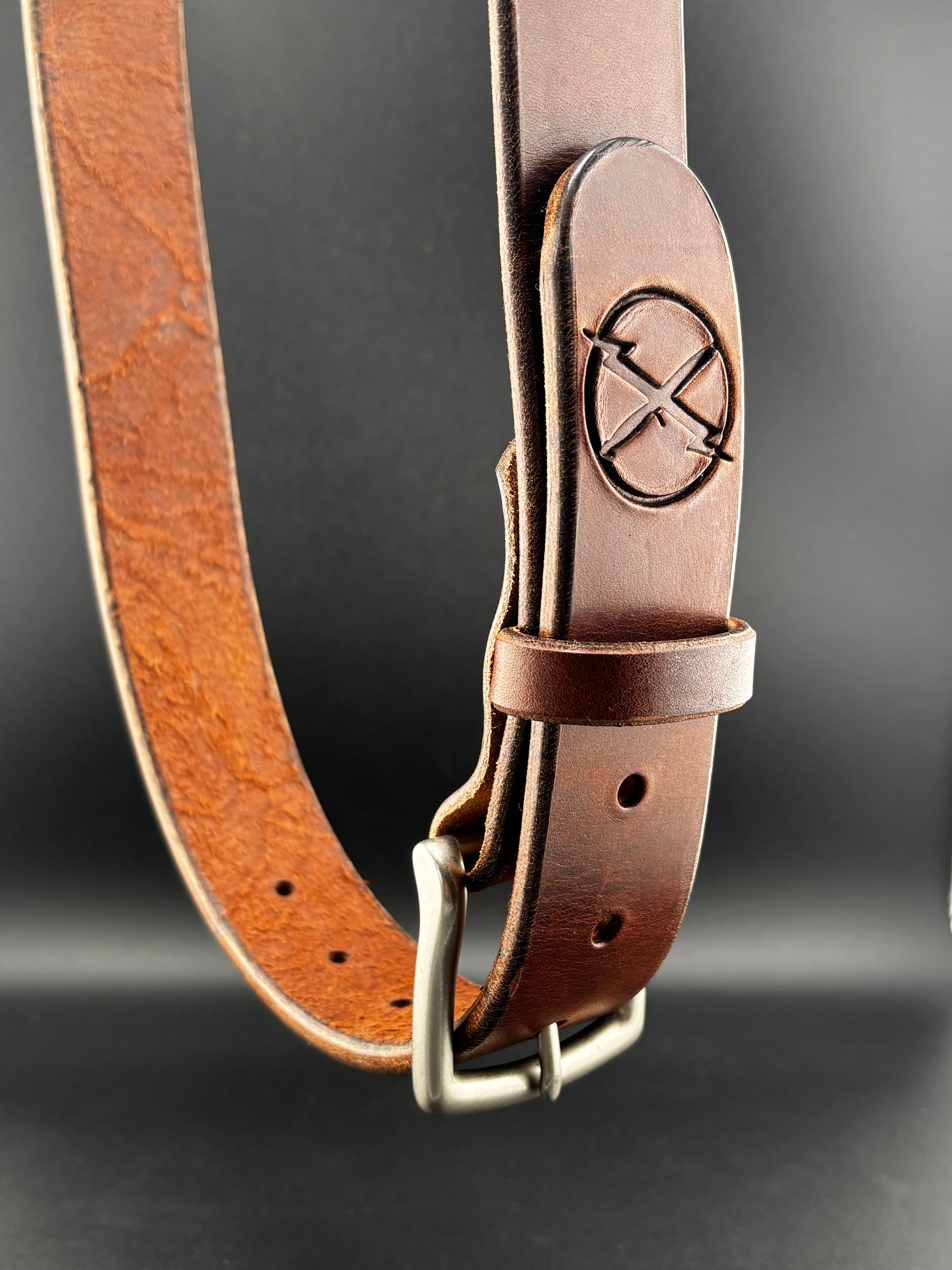 Brown leather belt with a metal buckle on a dark background