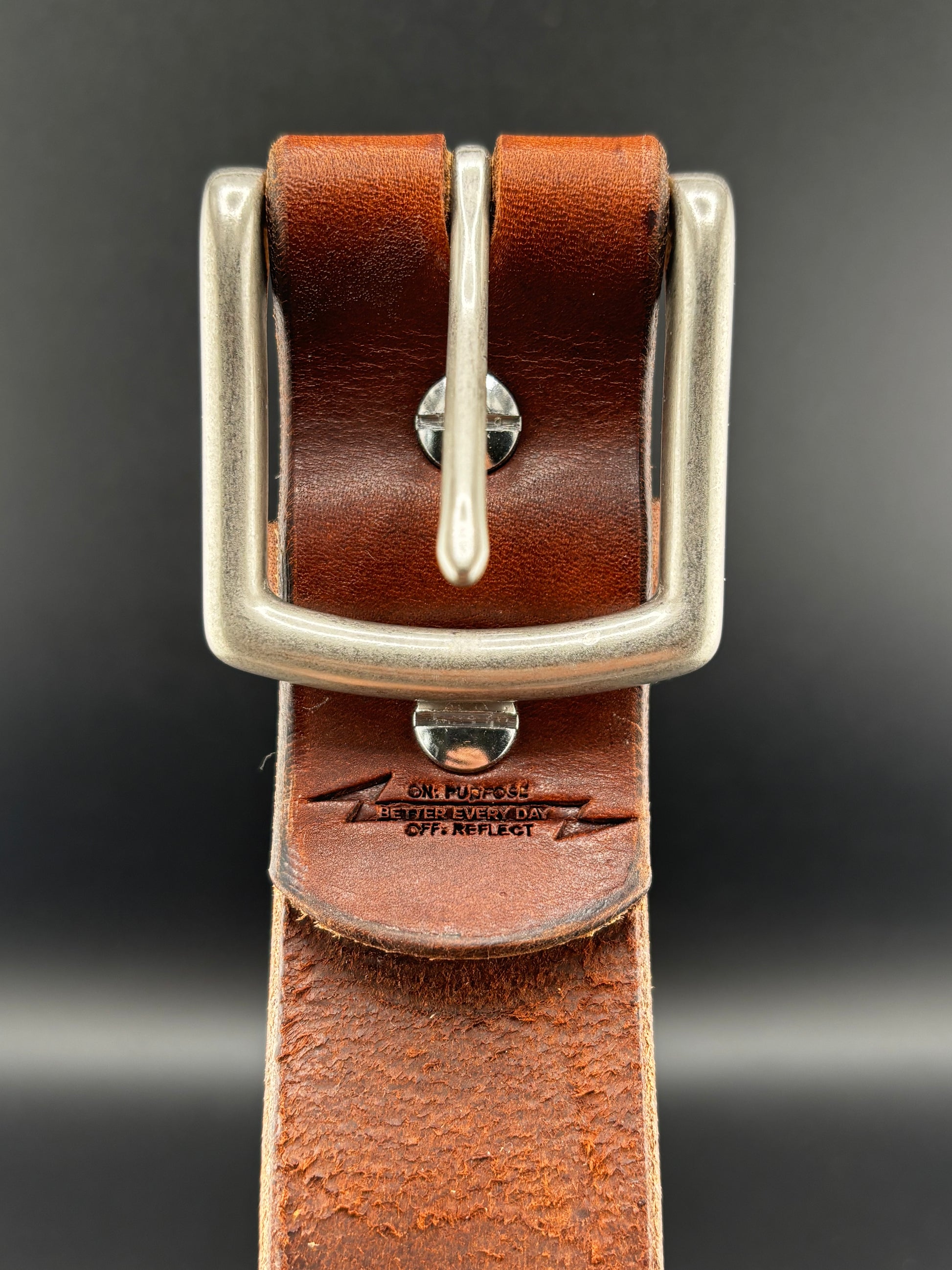 Brown leather belt with silver buckle on a dark background