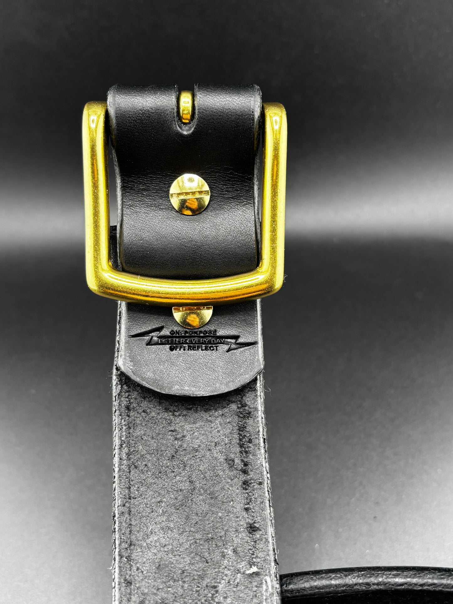 Black leather belt with a gold buckle on a dark background