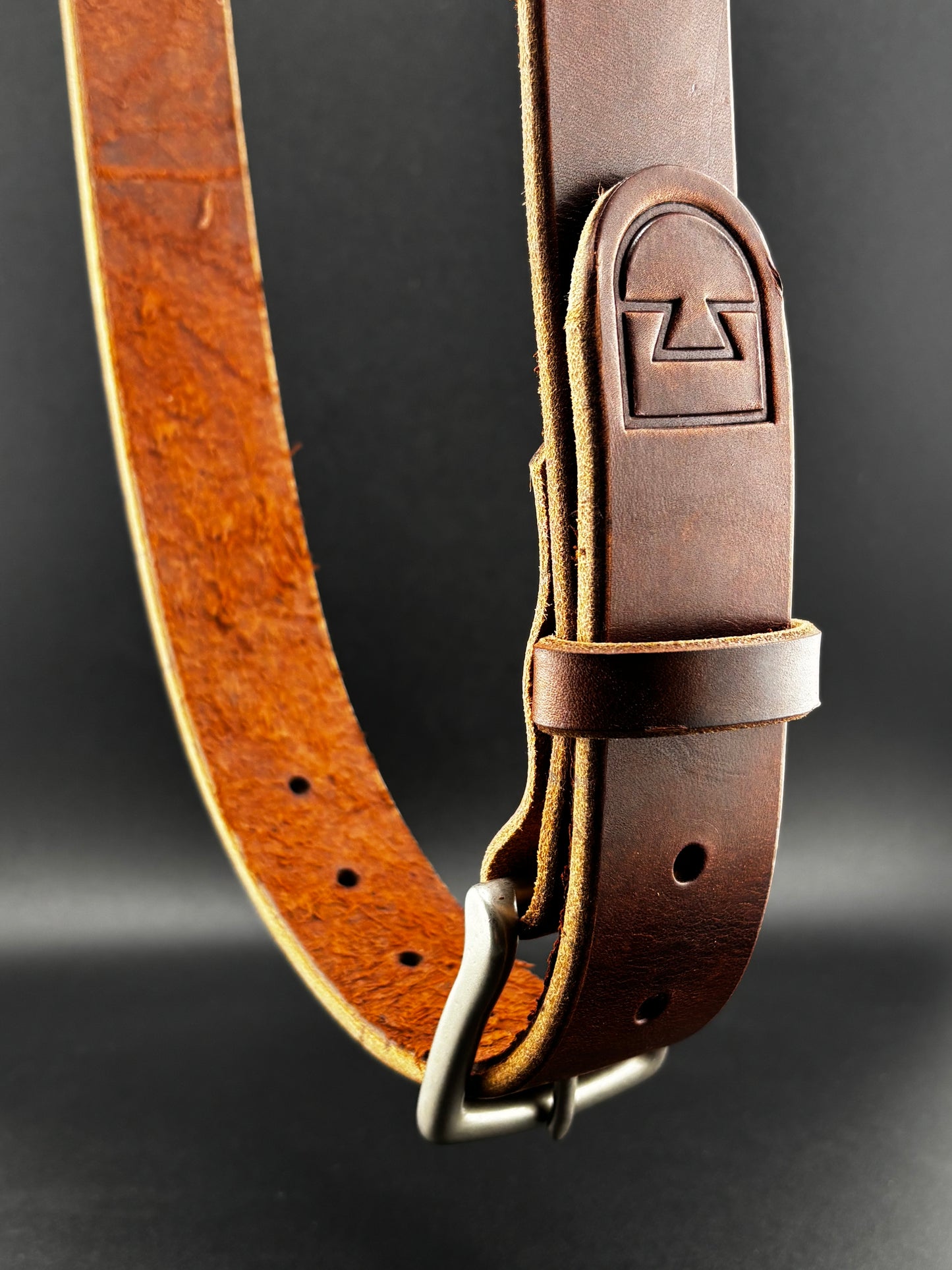 Brown leather belt with a metal buckle on a dark background